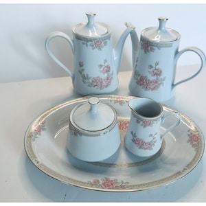 Puede incluir: Un juego de té de porcelana blanca con un diseño floral. El juego incluye una tetera, una jarra de crema, un azucarero y una bandeja de servir.