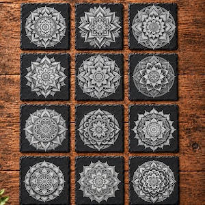 May include: A set of twelve square black slate coasters, each featuring a unique white mandala design. The coasters are arranged in a four-by-three grid pattern, showcasing intricate geometric patterns and symmetrical floral-like motifs.