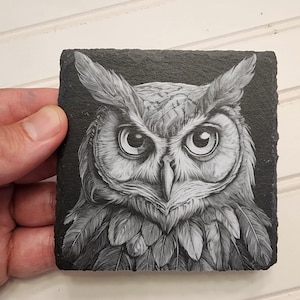 K&ouml;nnte beinhalten: Eine Schwarzwei&szlig;zeichnung einer Eule auf einem schwarzen Schieferuntersetzer. Die Augen der Eule sind gro&szlig; und rund, und ihre Federn sind detailliert.
