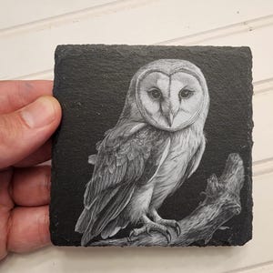K&ouml;nnte beinhalten: Eine Schwarzwei&szlig;zeichnung einer Schleiereule, die auf einem Ast sitzt, gedruckt auf einem schwarzen Schieferuntersetzer.