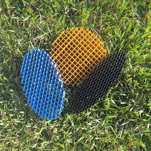 Puede incluir: Tres paneles de rejilla de plástico en azul, amarillo-naranja y negro descansan sobre hierba verde. Los paneles tienen un patrón cuadrado repetitivo. El panel azul es de forma ovalada, el amarillo-naranja es cuadrado y el negro es un rectángulo largo y estrecho.