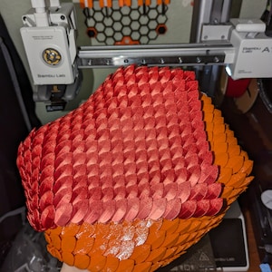 May include: A two-tone object with a scale-like texture, predominantly red at the top and transitioning to orange at the base. The object appears to be a decorative item or part of a larger design.