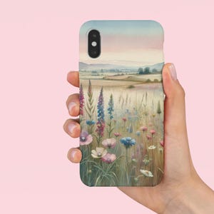 May include: A phone case with a watercolor painting of a field of wildflowers in shades of pink, blue, and purple. The background features a distant landscape with a hazy sky.
