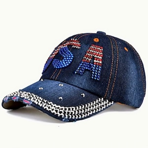 May include: A blue denim baseball cap with a rhinestoned "USA" design. The cap has a distressed brim and is decorated with silver studs.