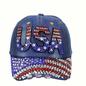 May include: A blue denim baseball cap featuring the letters USA in red, white, and blue rhinestones on the front panel. The brim is decorated with a rhinestone pattern resembling the American flag in red, white, and blue crystals.