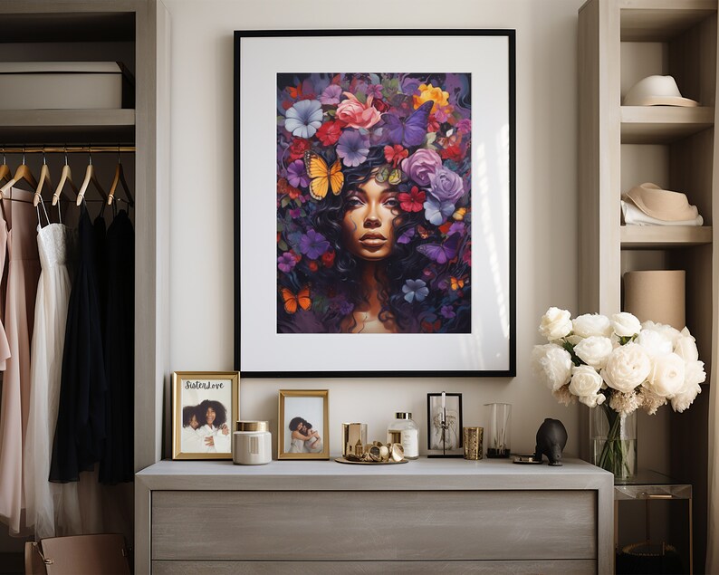 K&ouml;nnte beinhalten: Ein gerahmter Kunstdruck mit einer Frau mit Blumenschmuck und Schmetterlingen. Das Kunstwerk befindet sich in einem schwarzen Rahmen und wird auf einer grauen Kommode ausgestellt. Weitere Gegenst&auml;nde auf der Kommode sind gerahmte Fotos, Kerzen und dekorative Objekte.