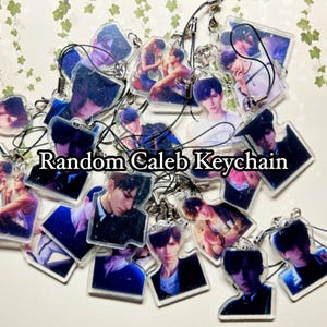 May include: A collection of clear acrylic keychains featuring various printed illustrations of a young person with dark hair, each attached to a black cord loop. The text Random Caleb Keychain is centered over the group of assorted character charms.
