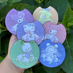 May include: A collection of six colorful car coasters featuring cartoon characters. Each coaster has a different design, including characters in shades of purple, pink, blue, green, and yellow. The coasters are round with a small notch.