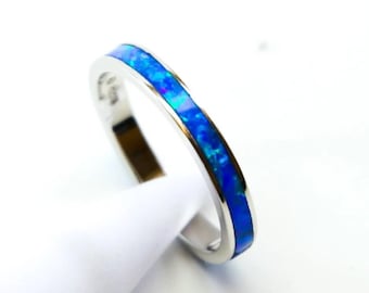Pode incluir: Um anel de prata com uma faixa de opala azul vibrante. A opala apresenta um padrão de mosaico de azuis e verdes. O anel está sobre um fundo branco, realçando o seu design.