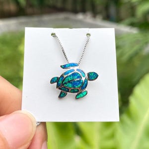 May include: A silver necklace featuring a turtle pendant with a vibrant blue and green opal-like design. The pendant is attached to a delicate chain, creating a striking piece of jewelry. The turtle pendant is approximately 1 inch in length.