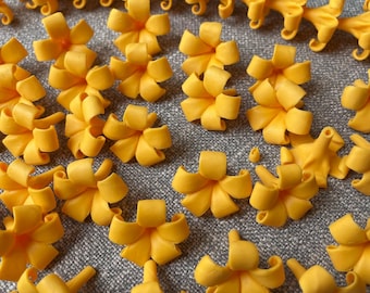 May include: A collection of bright yellow, bow-shaped floral decorations. Some are individual flowers, while others are connected in a chain. The flowers have a detailed, layered design, and are arranged on a gray surface.