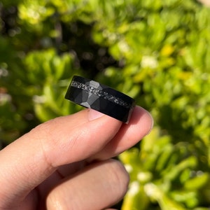 May include: A black tungsten carbide ring with a hammered finish and a thin band of silver-colored inlay.