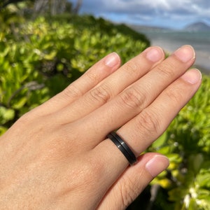K&ouml;nnte beinhalten: Nahaufnahme einer Hand, die zwei schwarze Ringe tr&auml;gt. Die Ringe sind schlicht und elegant, mit einer matten Oberfl&auml;che.