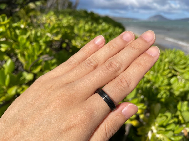 K&ouml;nnte beinhalten: Nahaufnahme einer Hand, die zwei schwarze Ringe tr&auml;gt. Die Ringe sind schlicht und elegant, mit einer matten Oberfl&auml;che.