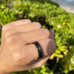 K&ouml;nnte beinhalten: Ein schwarzer Doppelring, der an einem Finger getragen wird.
