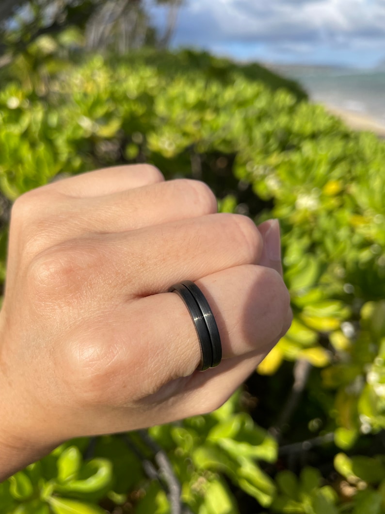 K&ouml;nnte beinhalten: Ein schwarzer Doppelring, der an einem Finger getragen wird.