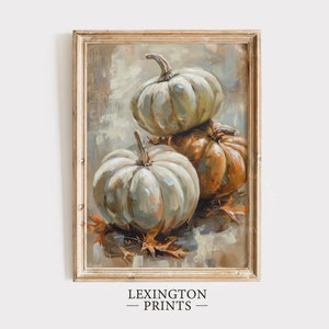 May include: A framed painting of three pumpkins, two white and one orange, with fall leaves on a textured background. The painting is in a light wood frame.