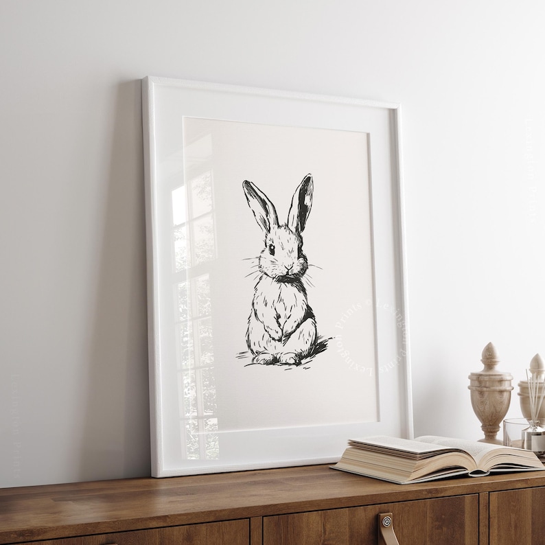Vintage black sketch wall art of a cute easter bunny rabbit. The sketch art print features thick black sketch work against a simple off white background. The sketch is a minimalist drawing fits an aesthetic for spring decor, easter decor, nursery decor, and rustic farmhouse decor. The shop name LexingtonPrints is written below