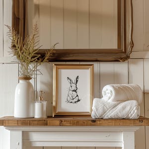 Vintage black sketch wall art of a cute easter bunny rabbit. The sketch art print features thick black sketch work against a simple off white background. The sketch is a minimalist drawing fits an aesthetic for spring decor, easter decor, nursery decor, and rustic farmhouse decor. The shop name LexingtonPrints is written below