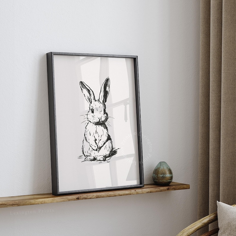 Vintage black sketch wall art of a cute easter bunny rabbit. The sketch art print features thick black sketch work against a simple off white background. The sketch is a minimalist drawing fits an aesthetic for spring decor, easter decor, nursery decor, and rustic farmhouse decor. The shop name LexingtonPrints is written below