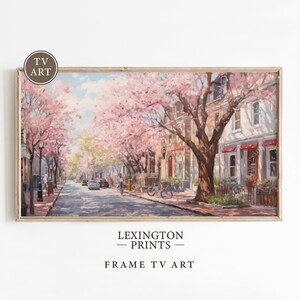 May include: A painting of a street lined with cherry blossom trees in full bloom. The trees are in the foreground, and the buildings are in the background. The street is paved with brick, and there are cars parked on the side of the street. The sky is blue and there are clouds in the sky.