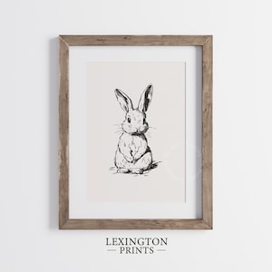 Vintage black sketch wall art of a cute easter bunny rabbit. The sketch art print features thick black sketch work against a simple off white background. The sketch is a minimalist drawing fits an aesthetic for spring decor, easter decor, nursery decor, and rustic farmhouse decor. The shop name LexingtonPrints is written below