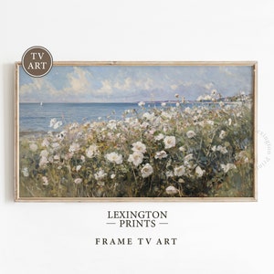 May include: A framed painting of a seascape with white flowers in the foreground. The sky is blue with white clouds and the sea is a deep blue. The flowers are in bloom and the painting is in a light wood frame.