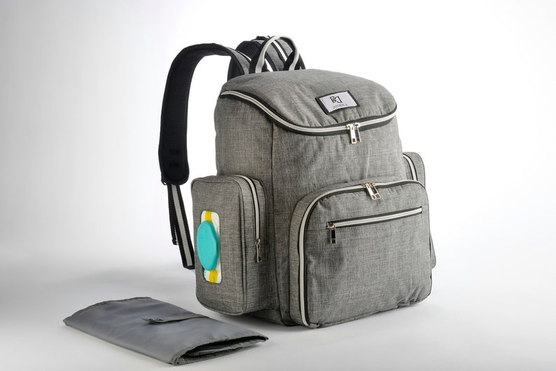 May include: A grey diaper bag backpack with multiple compartments and a changing mat. The bag has a top handle, padded shoulder straps, and a front pocket with a wipe dispenser. The bag has a white trim and gold zips.
