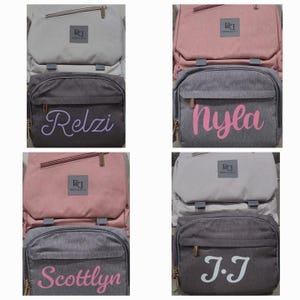 May include: Four gray and pink diaper bags with personalized names. The names are "Relzi", "Nyla", "Scottlyn", and "J.J".