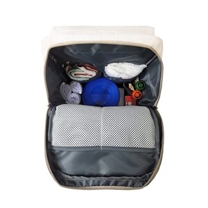 May include: A beige and gray diaper bag backpack with multiple pockets and compartments. The bag is open and filled with baby supplies, including diapers, wipes, a blue container, and other items.