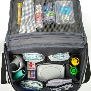 May include: Open black and grey baby changing bag packed with essentials. Contains nappies, wipes, bottles, a first aid kit, and toys. The bag has multiple compartments and a mesh top for easy viewing of contents.