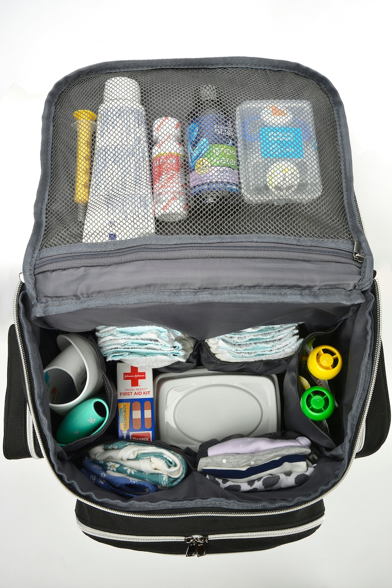 May include: Open black and grey baby changing bag packed with essentials. Contains nappies, wipes, bottles, a first aid kit, and toys. The bag has multiple compartments and a mesh top for easy viewing of contents.