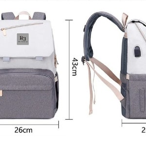 May include: A gray and white diaper bag backpack with a zippered pocket on the front. The bag has a large main compartment and a smaller pocket on the front. The bag is 26 inches wide, 20 inches deep, and 43 inches tall.