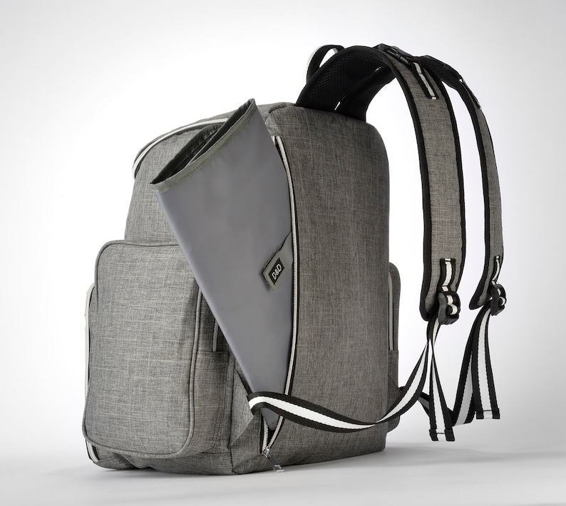 May include: Grey backpack with a changing mat. The backpack features multiple pockets and a zip closure. The shoulder straps are black and white striped. The changing mat is grey and has the letters "D&D" on it.