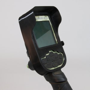 May include: Black metal detector control unit with a green screen and a sunshade. The control unit has a keypad with several buttons.