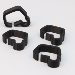 May include: Four black plastic cable organizers shaped like a van. The organizers are designed to hold and organize cables.