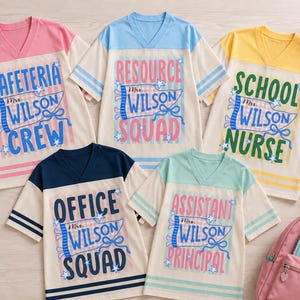 May include: Five v-neck t-shirts with cream bodies and colored sleeves. Each shirt features a blue pennant graphic with the text Mrs. Wilson and unique titles: Cafeteria Crew, Resource Squad, School Nurse, Office Squad, and Assistant Principal.
