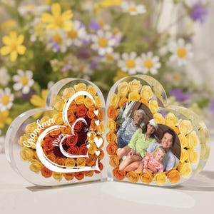 May include: A heart-shaped photo frame with a clear acrylic exterior. The left side features a heart design with the words "Grandma", "Mom", and names, surrounded by orange and yellow roses. The right side holds a family photo.