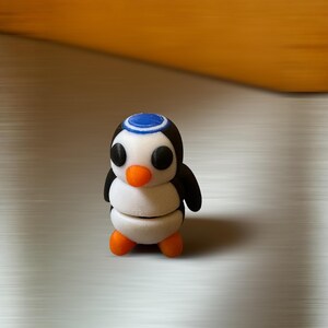 May include: A small, white penguin figurine with black wings and a blue and white hat. The penguin has orange feet and black eyes.