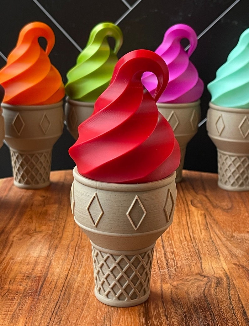 May include: Five ice cream cones with different colored ice cream. The cones are all brown and have a waffle pattern. The ice cream is red, green, orange, purple, and blue.