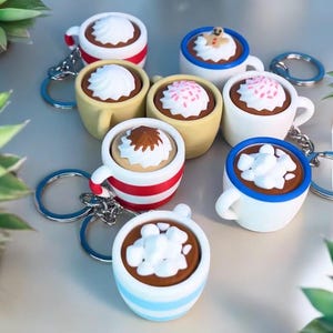 May include: A set of seven colorful, miniature ceramic mugs with different toppings, such as whipped cream, marshmallows, sprinkles, and gingerbread men. Each mug is attached to a silver key chain.