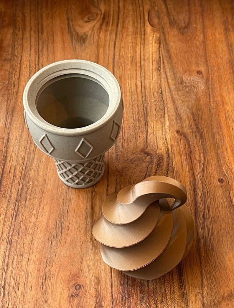 May include: A brown ceramic ice cream cone with a white ceramic ice cream scoop on top. The ice cream cone is sitting on a wooden surface.