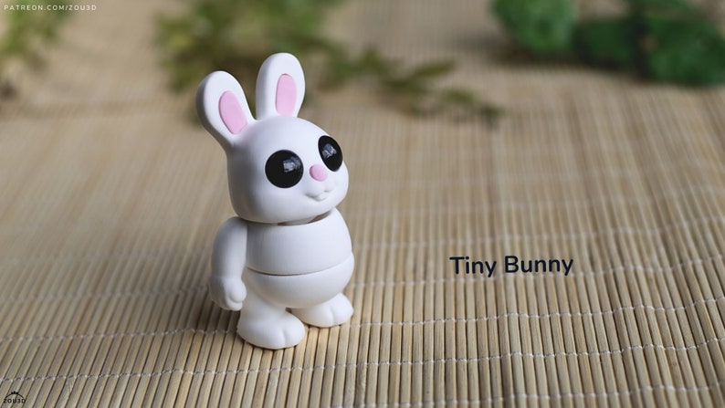 May include: A white, segmented, articulated toy bunny with black eyes and pink ears. The bunny is standing on a woven bamboo mat. The text "Tiny Bunny" is visible in the image.