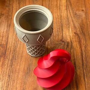 May include: A gray ice cream cone with a red swirl of ice cream on top. The cone is made of plastic and has a waffle pattern.