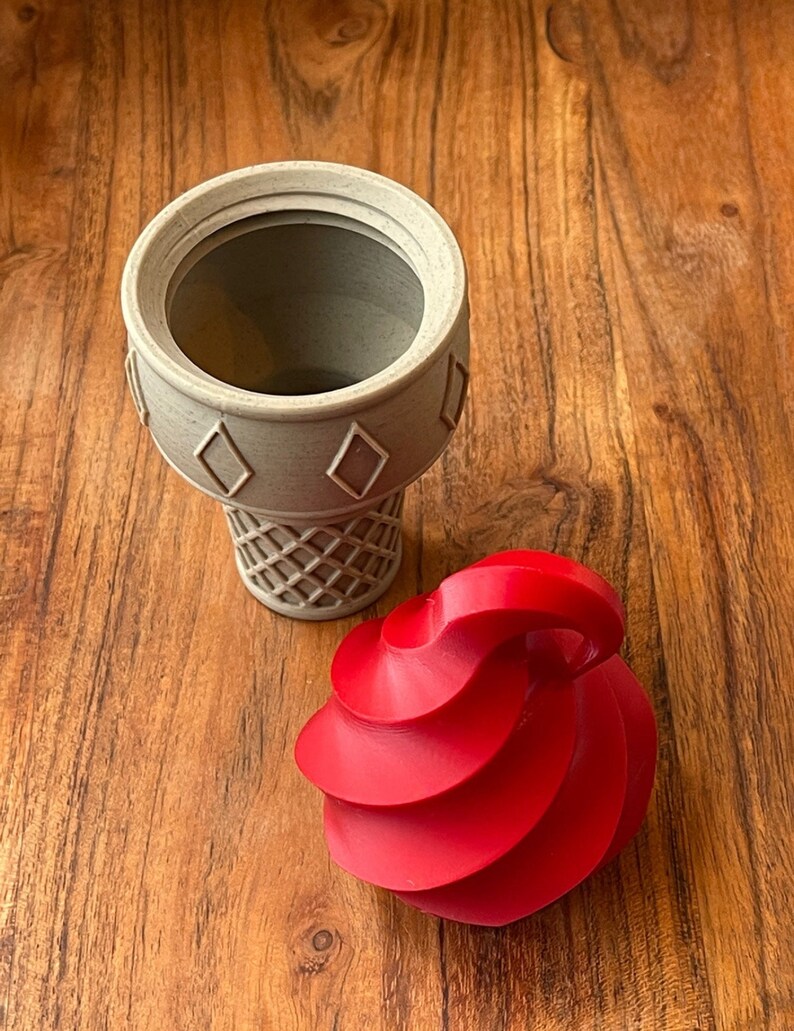 May include: A gray ice cream cone with a red swirl of ice cream on top. The cone is made of plastic and has a waffle pattern.