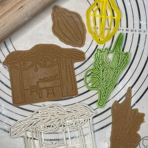 Puede incluir: Un juego de cinco cortadores de galletas para hacer galletas con temática de Sucot. Los cortadores están hechos de plástico blanco y presentan diseños de una sucá, un lulav, un etrog, un dátil y una rama de palmera.