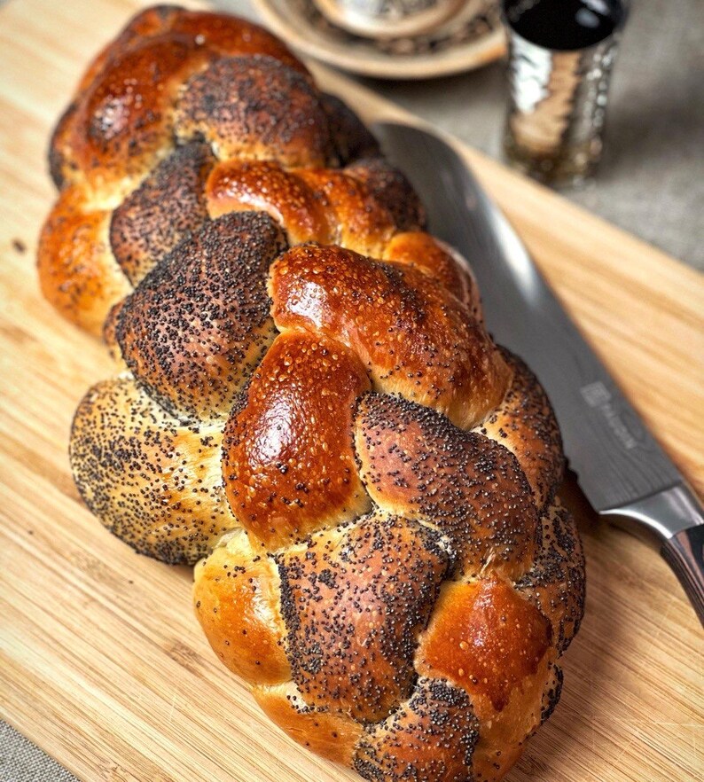 May include: A braided loaf of bread with poppy seeds on a wooden cutting board. The bread is golden brown and has a shiny glaze.