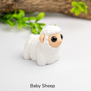 Puede incluir: Figura de oveja beb&eacute; blanca con grandes ojos negros y orejas marrones. La oveja est&aacute; hecha de un material liso. El texto "Baby Sheep" est&aacute; impreso debajo.