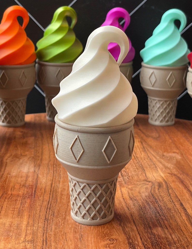 Op de afbeelding: Een witte swirl-ijscone met een bruine wafeltje. Het ijs is in de vorm van een swirl en staat op een houten tafel. Er zijn andere ijscones op de achtergrond, maar die zijn wazig.