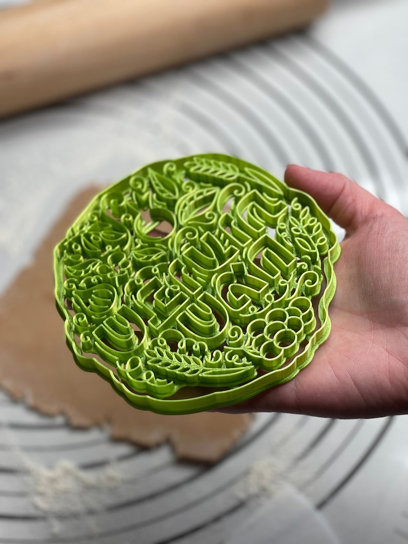 May include: Green plastic cookie cutter with a detailed design featuring the words "Be Kind" surrounded by leaves and vines.